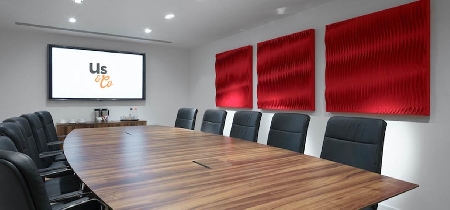 A wooden conference table with ten chairs and a large screen on the wall