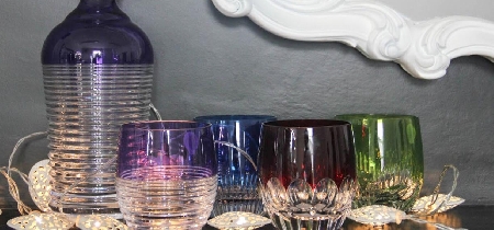 An assortment of coloured drinking glasses with a coloured glass decanter