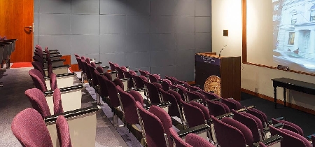 An empty lecture theatre with tiered seating and an image of a building projected on the screen